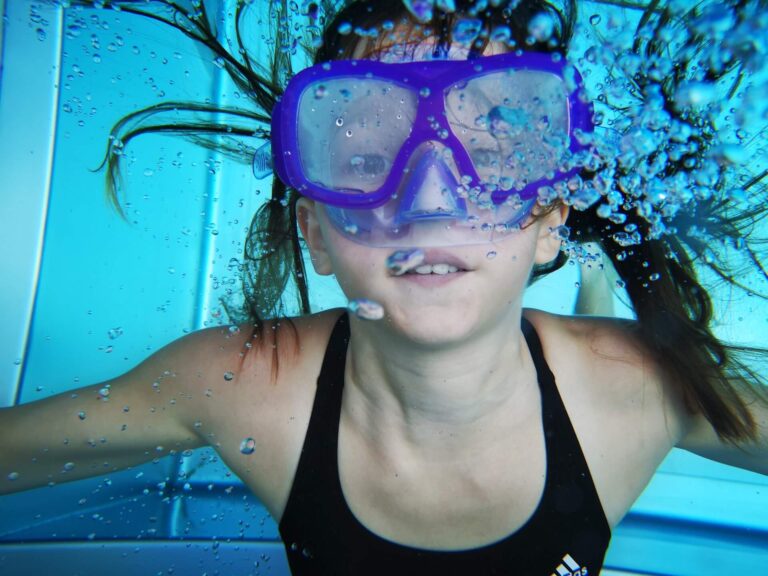 young girl swimming underwater with snorkel goggles on